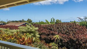 Uitzicht vanaf een balkon op een aangelegde tuin met diverse planten en een verderop gelegen huizen.