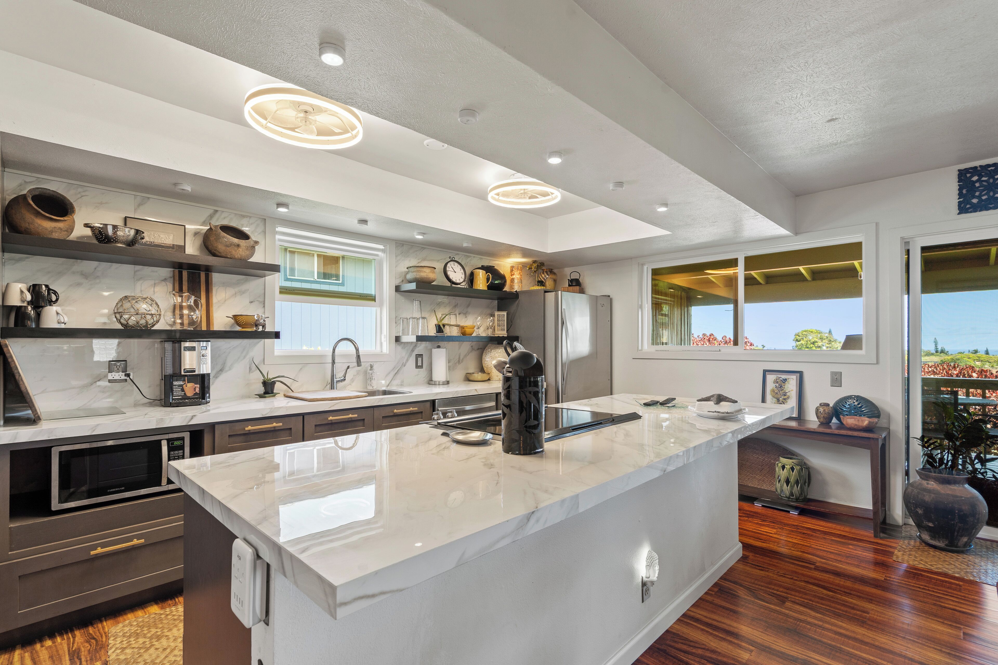A modern kitchen with marble countertops, built-in appliances, and decorative items on shelves.