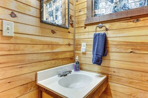 Ein Badezimmer mit Holzwandverkleidung, einem weißen Waschbecken, einem Spiegel, einem Handtuchhalter und einer Seifenspender.