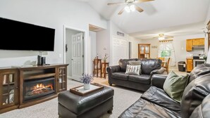 A living room with a fireplace, leather sofas, a flat-screen TV, and a ceiling fan. - Welcome to “Whimsy Woods Cabin” – The Ultimate Cabin Retreat on Lake Cumberland (Burnside)