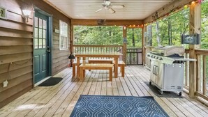 A wooden deck with a table and benches, a grill, and a view of the forest. - Welcome to “Whimsy Woods Cabin” – The Ultimate Cabin Retreat on Lake Cumberland (Burnside)