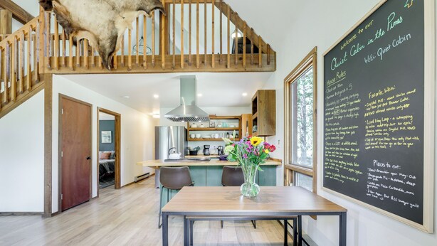 A modern kitchen with a wooden staircase, a dining table with a vase of flowers, and a chalkboard with house rules and favorite hikes. - Steps to Crystal River: Hideaway w/ Mountain Views (Marble)