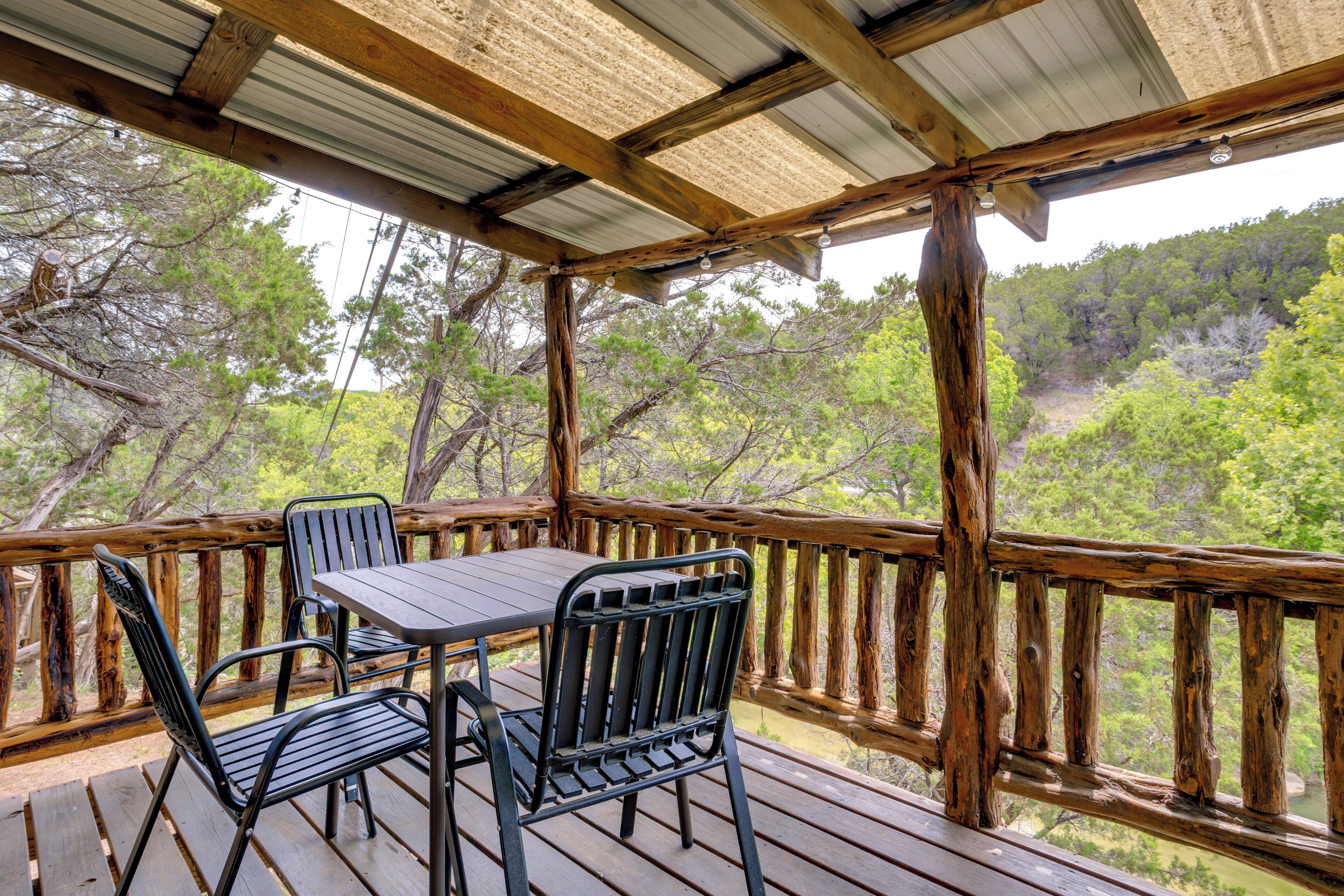 A wooden deck with a table and chairs, overlooking a forested area.