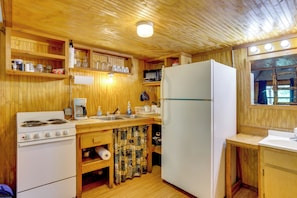 A wooden-paneled kitchen with a stove, microwave, refrigerator, and wooden shelves. - Cedar Falls Cabin 2: Family Getaway By Honey Creek (Davis)