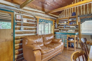 Interior de una cabaña de troncos con un sofá de cuero, repisas de madera y un cartel de recepción.