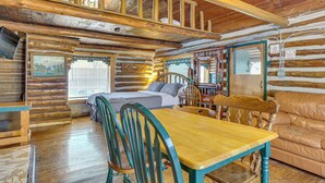 Ein rustikales Blockhaus mit Holzesstisch, Stühlen, einer Couch, einem Bett und einer Treppe.