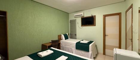 A hotel room with two beds, a desk, an air conditioning unit, a television, and a door.
