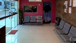 A hotel lobby with a chandelier, a reception desk, a waiting area with chairs, and a wall-mounted air conditioning unit.