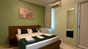 A bedroom with a wooden bed, green bedding, a wall-mounted air conditioner, a mirror, and a painting on the wall.