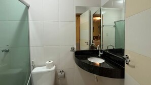 A bathroom with a toilet, a sink, a mirror, and a shower enclosure.