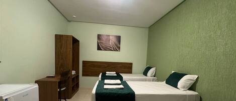 Een kamer met twee bedden, een bureau, een kledingkast en een kleine koelkast.