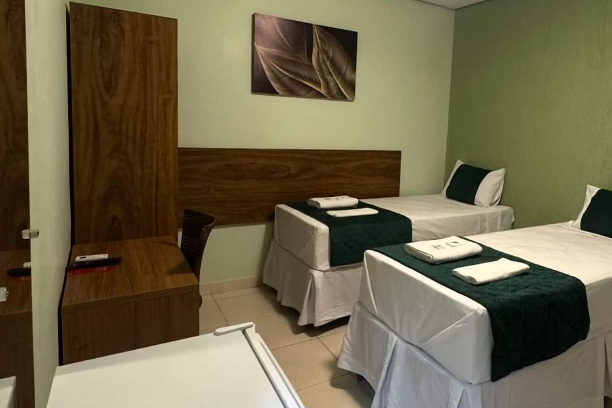 A hotel room with two beds, a wooden headboard, a painting, a desk, and a refrigerator.
