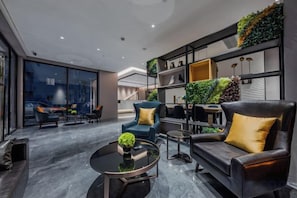 A modern living room with a sofa, armchair, and coffee table. There is a large window with a view of the city.