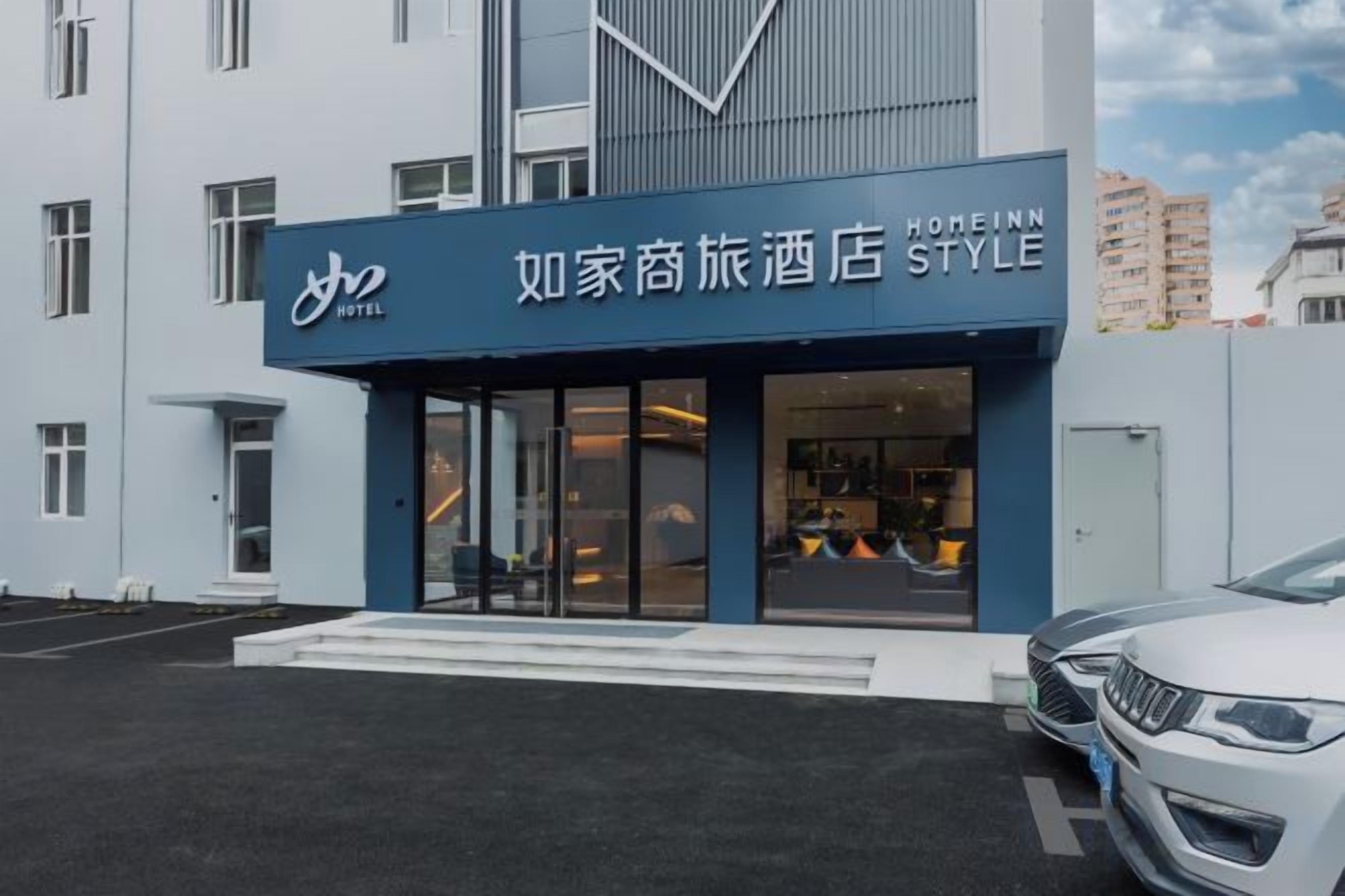 A hotel entrance with a modern facade, a clear glass door, and a parking area with a white car.
