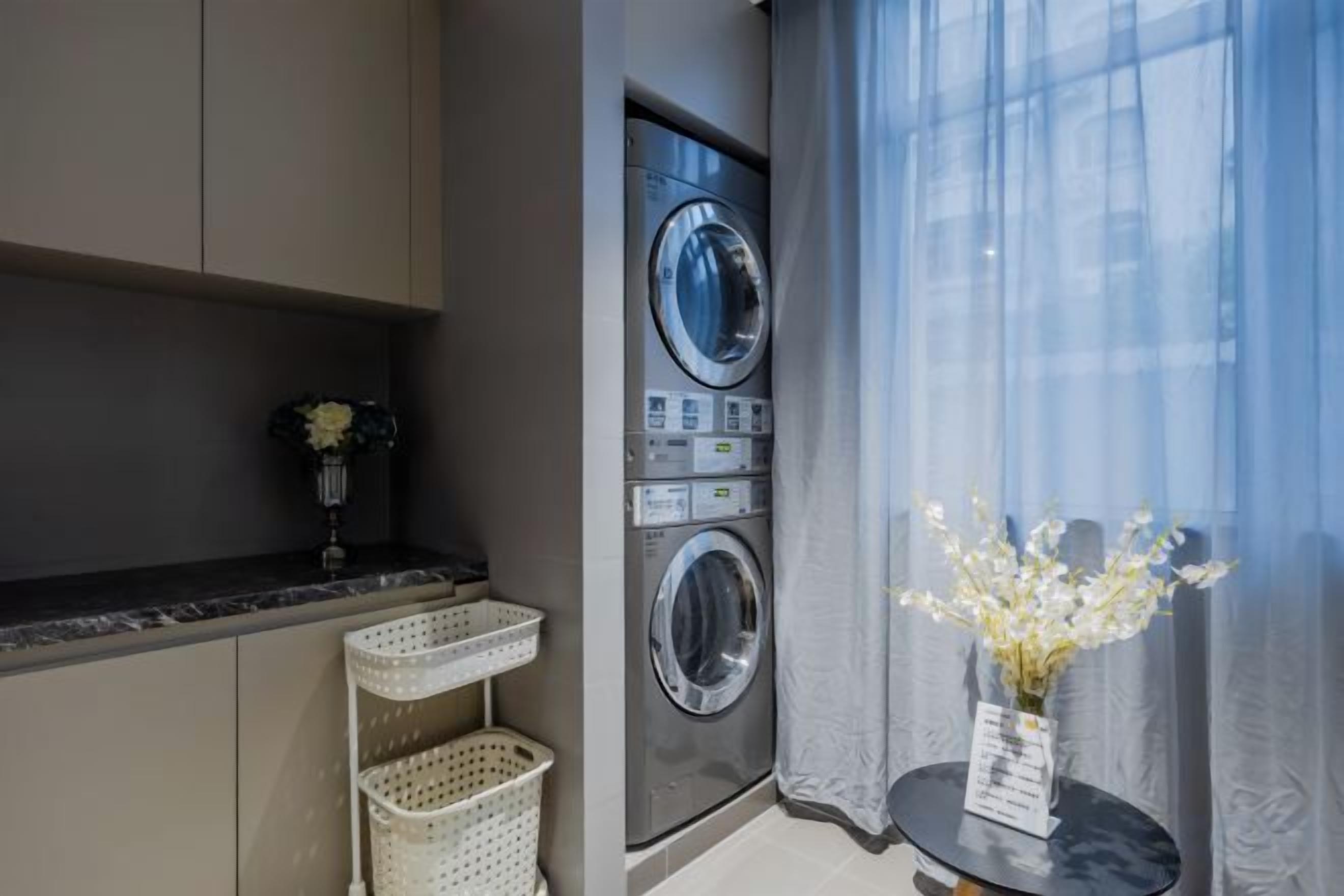 A compact laundry area with a washing machine, a dryer, and a small table with a vase of flowers.