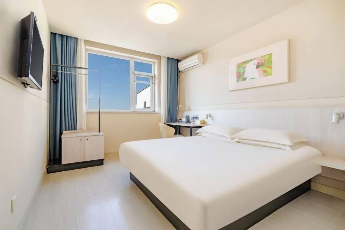 Habitació d'hotel amb un llit gran, un televisor fixat a la paret, una finestra amb cortines i una taula petita amb una cadira.