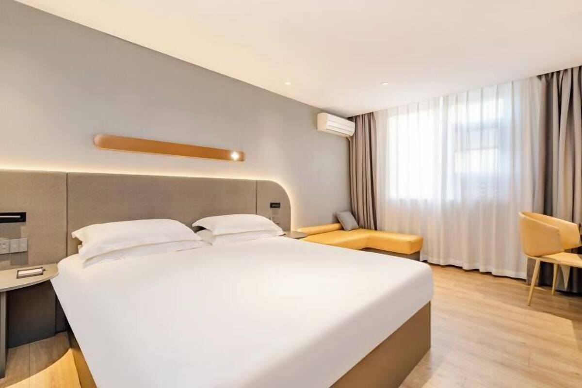 Una habitació d'hotel moderna amb un llit gran, una taula de nit, una cadira i una finestra amb cortines.