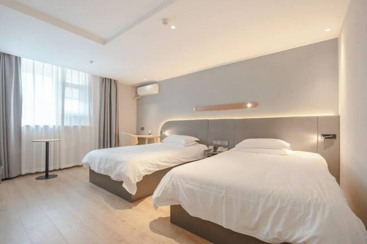 Habitació d'hotel moderna amb dos llits, una taula petita i una finestra gran amb cortines.