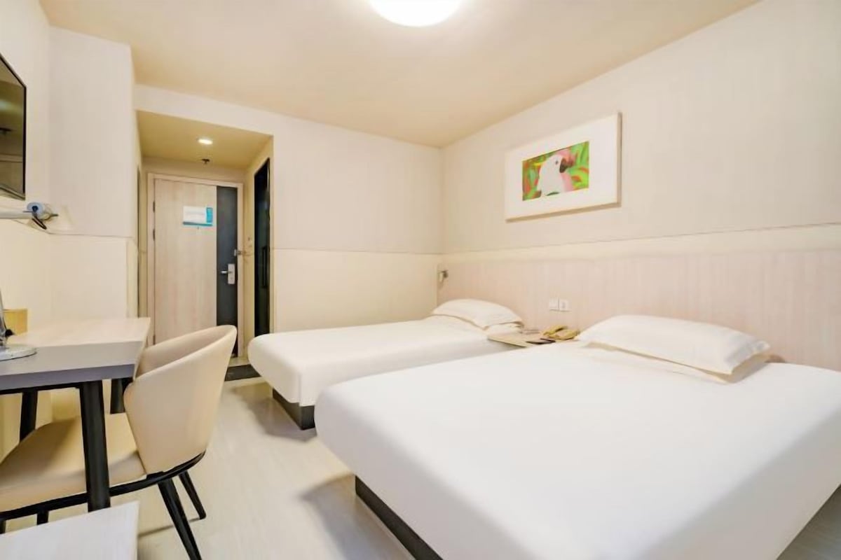 A hotel room with two single beds, a desk, and a chair.