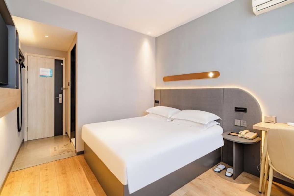 Una habitación de hotel con cama, mesita de noche, lámpara y una puerta que da a otra habitación.