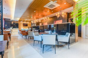 A modern restaurant with wooden ceiling panels, pendant lighting, and a central dining area with tables and chairs.