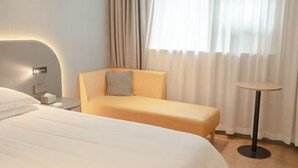 A hotel room with a bed, a sofa, a small table, and a window with curtains.