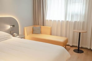A hotel room with a bed, a sofa, a small table, and a window with curtains.