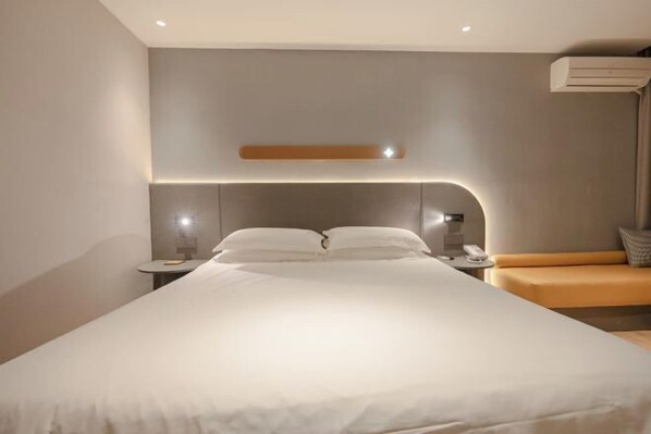 A modern hotel room with a large bed, a bedside table with a lamp, and a small seating area with a cushion.