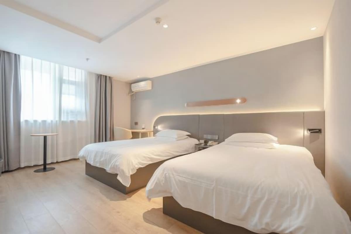 A modern hotel room with two beds, a small table, and a large window with curtains.
