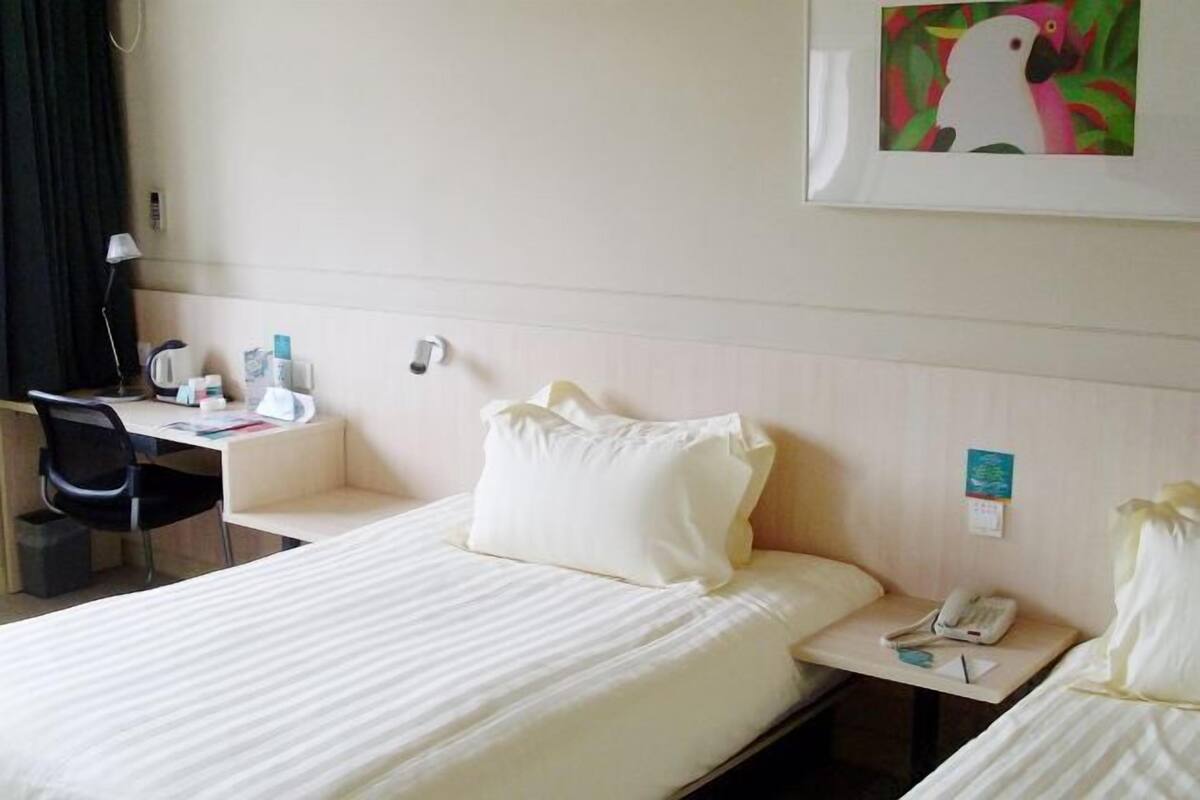 Una habitació d'hotel amb un llit, una taula, una cadira, un telèfon i un quadre al mur.