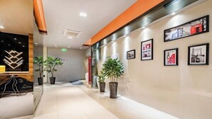 Een moderne hotel lobby met een strak betegelde vloer, potplanten en ingelijste foto's aan de muur.