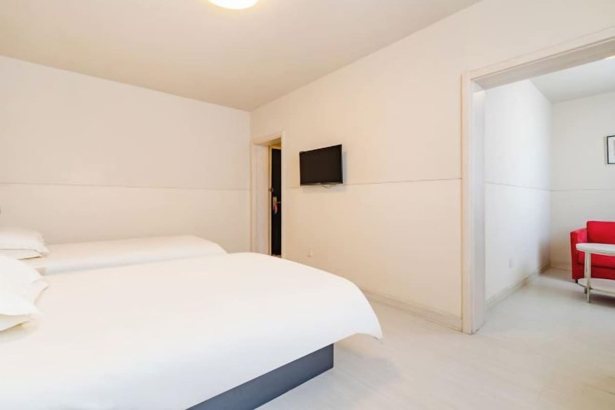 Una habitación de hotel moderna con una cama grande, un televisor de pantalla plana en la pared y una silla roja en la esquina.