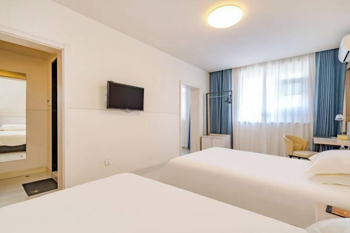 Habitació d'hotel amb dos llits, una televisió penjada a la paret, escriptori amb cadira i finestra amb cortines.