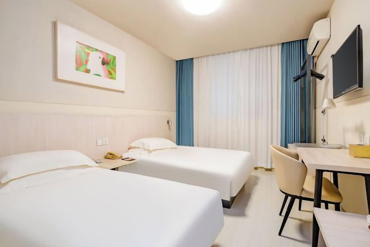 A hotel room with two beds, a desk, a chair, a TV, and a window with curtains.