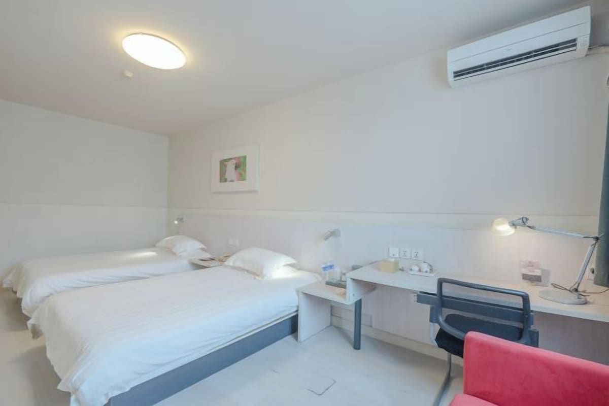 Una habitación de hotel con dos camas, un escritorio con una silla, una lámpara de escritorio y un equipo de aire acondicionado.