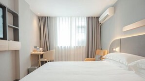A hotel room with a large bed, a desk with a chair, a TV mounted on the wall, and an air conditioning unit.