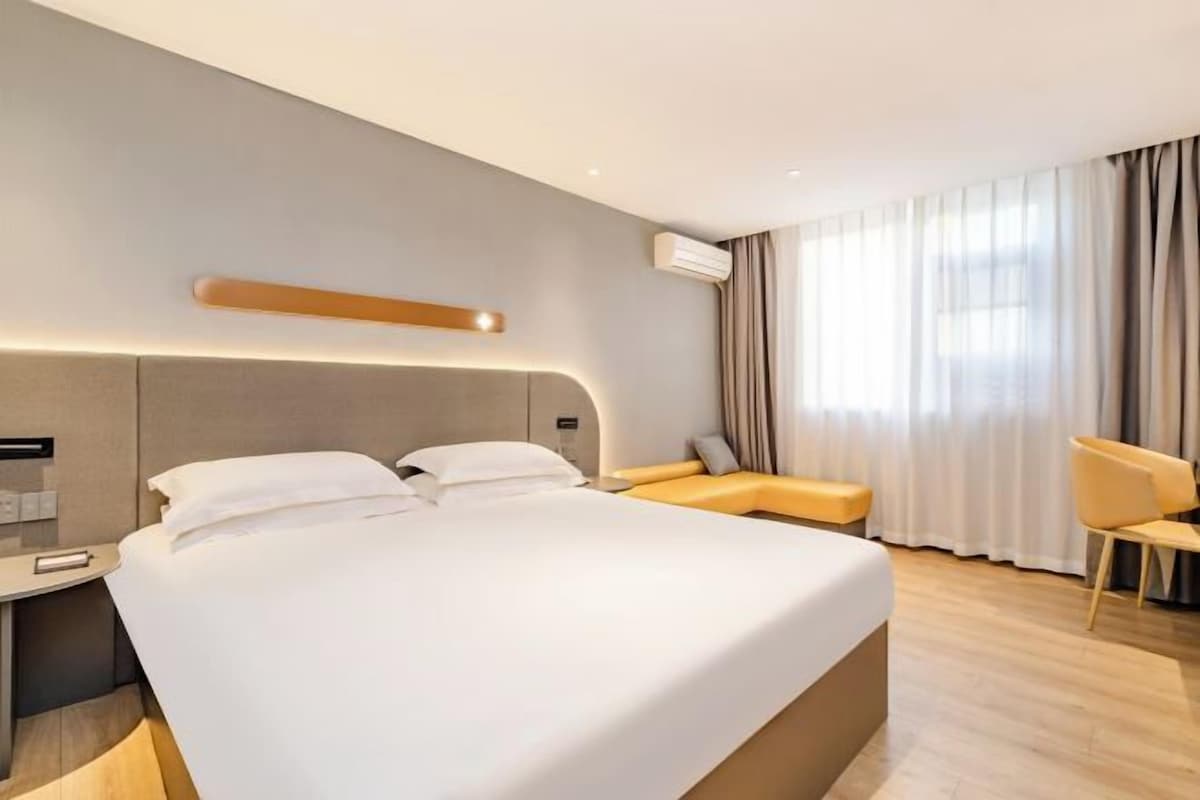 A modern hotel room with a large bed, a bedside table, a chair, and a window with curtains.