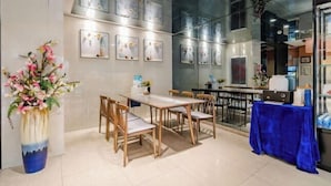 Een moderne eethoek met een lange tafel en stoelen, een blauwe tafelkleed en lijstwerken aan de wanden.