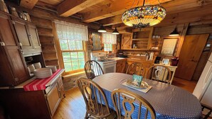 A wooden cabin interior with a dining table, chairs, a chandelier, and a kitchen area. - Gibby's Log Cabin Retreat (Washington)