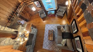 A cozy log cabin interior with a stone fireplace, a wooden ceiling, and a checkered armchair. - Gibby's Log Cabin Retreat (Washington)