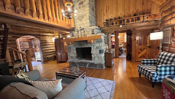 A cozy log cabin interior with a stone fireplace, wooden furniture, and a staircase leading to the upper level. - Gibby's Log Cabin Retreat (Washington)