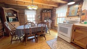 A wooden cabin interior with a dining table, chairs, a stove, and a chandelier. - Gibby's Log Cabin Retreat (Washington)