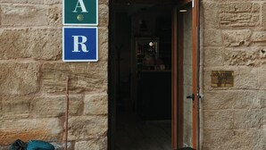Un edificio in pietra con un cartello che indica “RESTAURANTE” e segnaletica per parcheggio con posti contrassegnati da “A” e “R”.