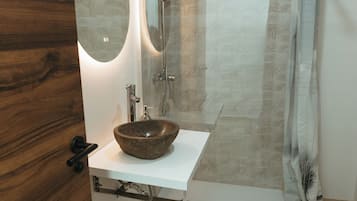 A bathroom with a wooden floor, a white sink with a stone basin, a mirror, and a shower with a patterned curtain.