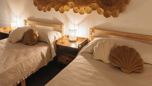 Due letti singoli con testiere in legno, un pannello decorativo intrecciato sopra e un comodino con una lampada.