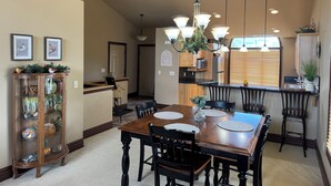 A dining area with a wooden table, black chairs, a chandelier, and a kitchen in the background. -  Cozy Fairway Retreat - Near Ski, Golf & Town (Red Lodge)