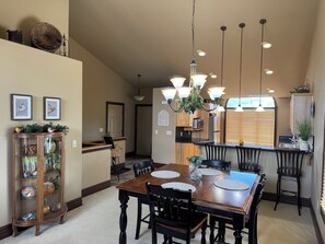 A dining area with a wooden table, black chairs, a chandelier, and a kitchen in the background. -  Cozy Fairway Retreat - Near Ski, Golf & Town (Red Lodge)