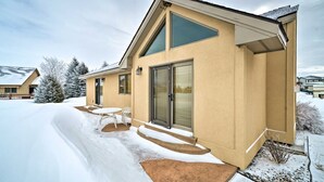 A modern house with a large glass door, a covered patio with outdoor furniture, and a snow-covered driveway. -  Cozy Fairway Retreat - Near Ski, Golf & Town (Red Lodge)