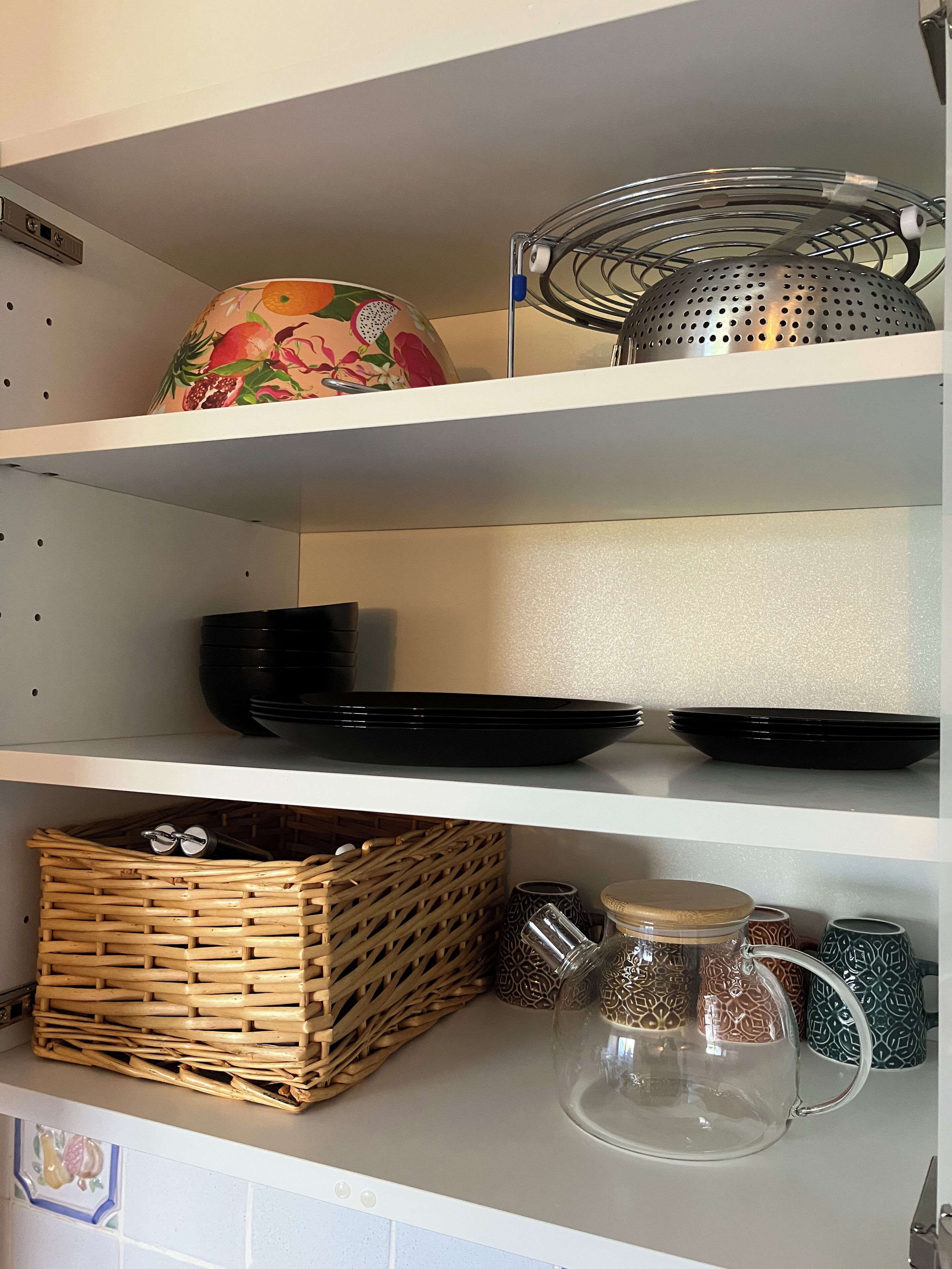 A kitchen shelf with black plates, a colander, and a wicker basket.
