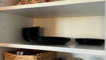 A kitchen shelf with black plates, a colander, and a wicker basket.
